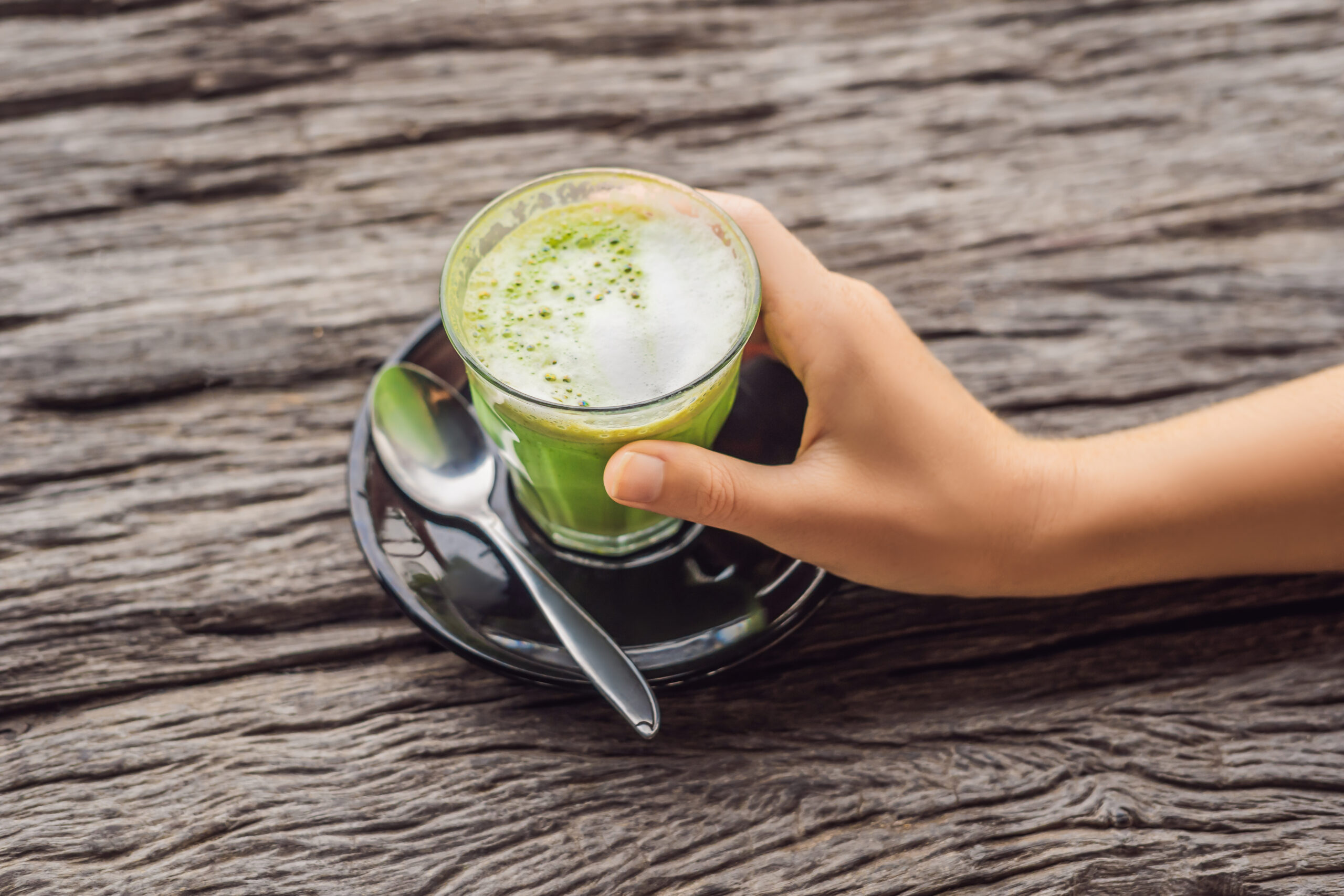Women's Hand holding cup of matcha Latte, Green Tea, on old Wooden Background table