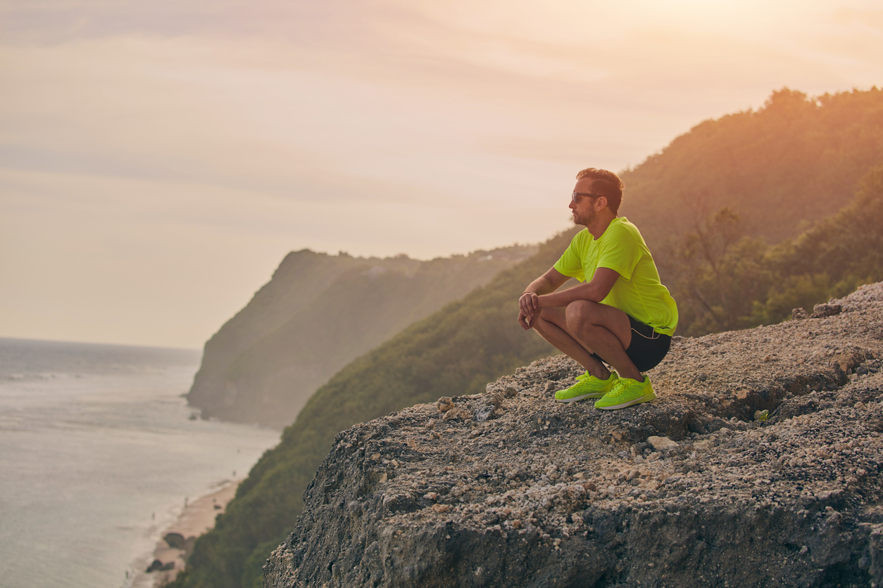 Sportsman making pause after workout on a tropical cliff.